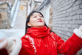 雪后在老城古巷穿着喜庆服饰的亚洲少女