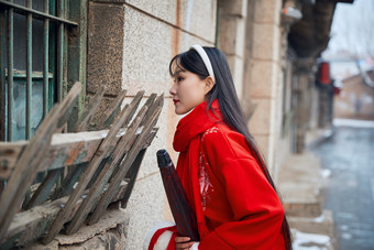 雪后在老城古巷穿着喜庆服饰的亚洲少女