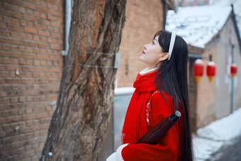 雪后在老城古巷穿着喜庆服饰的亚洲少女