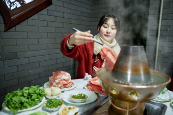 在饭店吃传统铜锅涮肉的亚洲少女