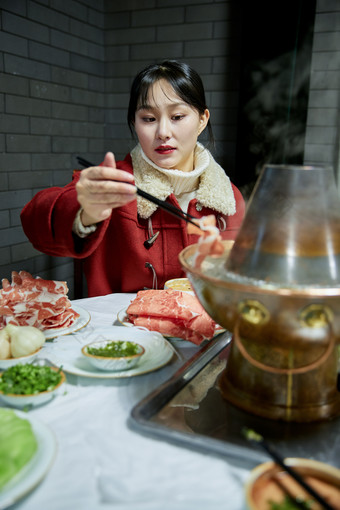 在饭店吃传统铜锅涮肉的亚洲少女