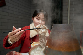 在饭店吃传统铜锅涮肉的亚洲少女