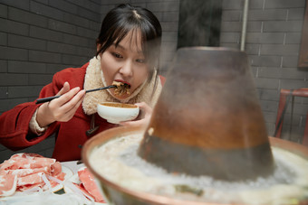 在饭店吃传统铜锅涮肉的亚洲少女