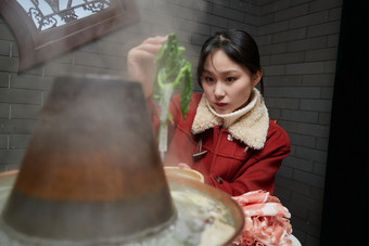 在饭店吃传统铜锅涮肉的亚洲少女