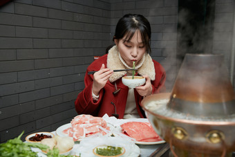 在饭店吃传统铜锅涮肉的亚洲少女