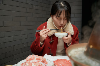 在饭店吃传统铜锅涮肉的亚洲少女