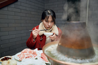 在饭店吃传统铜锅涮肉的亚洲少女