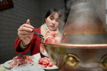 在饭店吃传统铜锅涮肉的亚洲少女