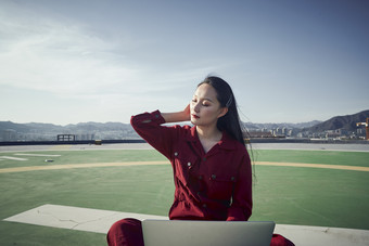 亚洲商务年轻女性在楼顶停机坪使用电脑办公