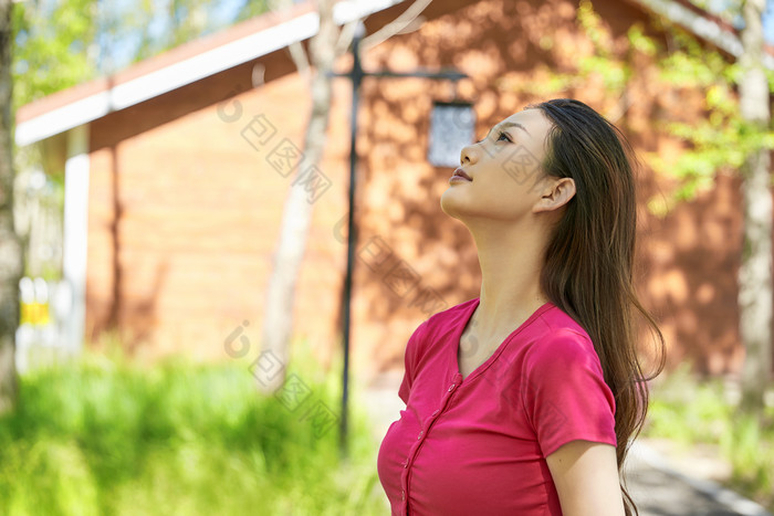 站在绿草如茵的木屋别墅群外的东方美女