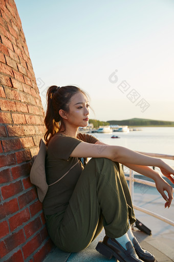 盛夏夕阳晚霞湖边码头灯塔上的少女