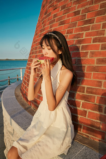 盛夏夕阳湖边码头灯塔上吃西瓜的少女