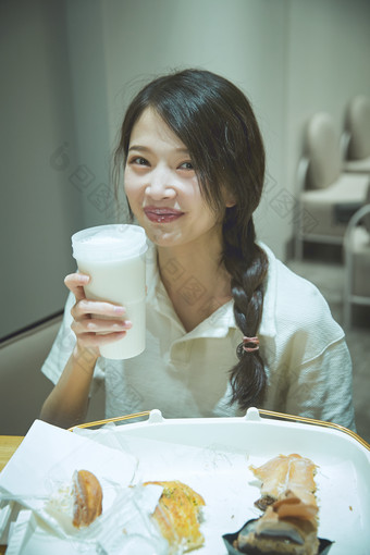 在烘焙店吃面包喝牛奶的可爱亚洲少女