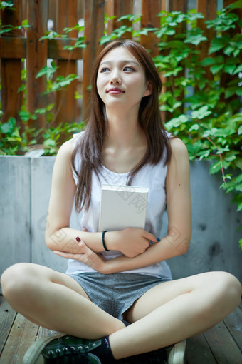 院子里坐在长椅上阅读书籍的亚洲长发少女