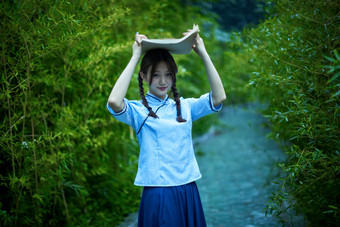 细雨中庭院里竹林前怀抱古书籍的民国风少女