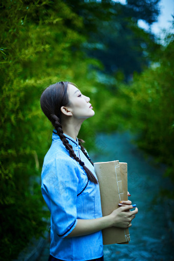 细雨中庭院里竹林前怀抱古书籍的<strong>民国风</strong>少女