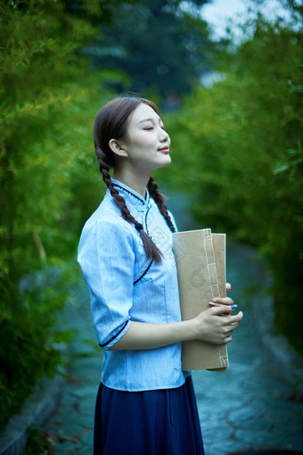 细雨中庭院里竹林前怀抱<strong>古书</strong>籍的民国风少女