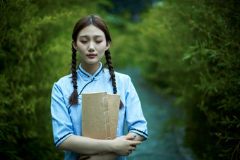 细雨中庭院里竹林前怀抱古书籍的民国风少女