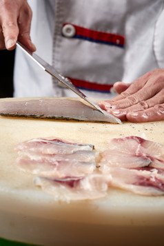 白色砧板上厨师用精湛的刀工展示生鱼片及鲜鱼料理切割分切的刀工
