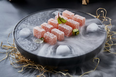 干冰缭绕的黑瓷餐具摆放的番茄糖霜江米糕