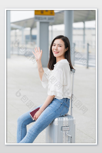 坐在行李箱上挥手的年轻美女摄影图片