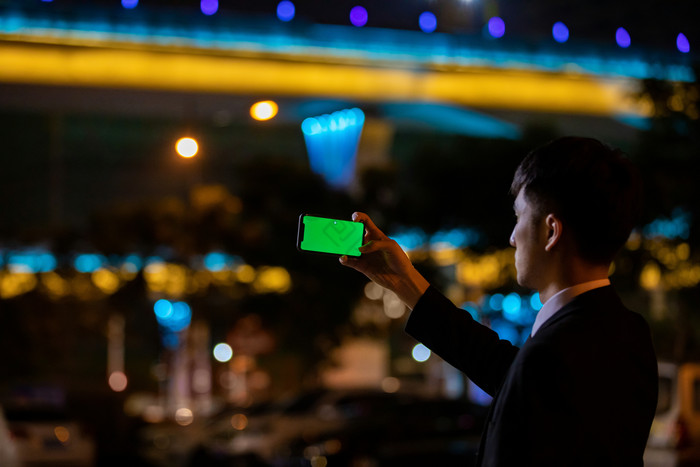 商务西装男绿屏手机拍摄夜景可做特效摄影图图片