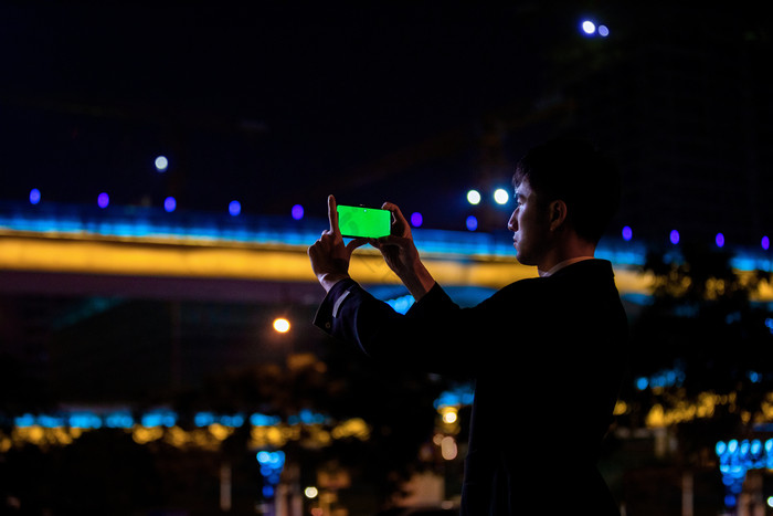 商务西装男手机拍摄绿屏画面夜景摄影图图片