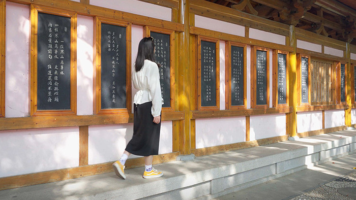 4K实拍美女走在寺庙长廊用手抚摸墙上的字