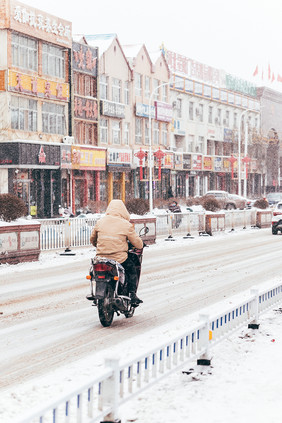 城市大雪中骑摩托车的行人实拍摄影图