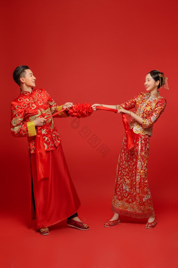 穿着中式传统婚服的新人拉扯绣球图片