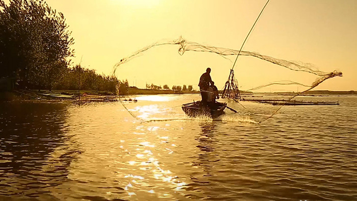 夕阳下渔民湖边撒网捕鱼