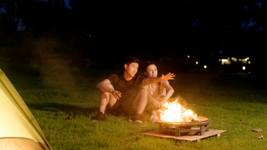 夜晚露营篝火旁相谈甚欢的青年男女实拍