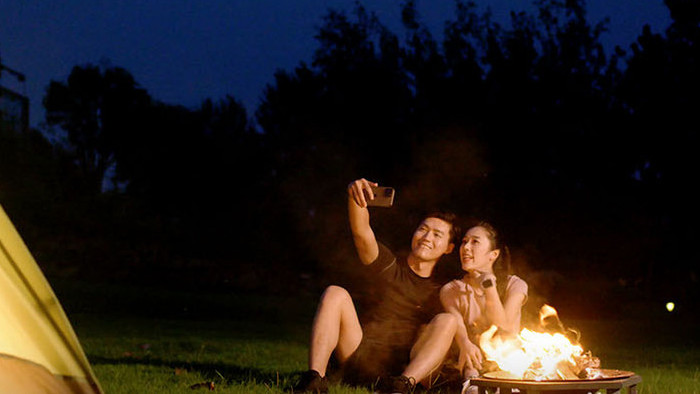 夜晚露营拿出手机自拍的年轻情侣实拍