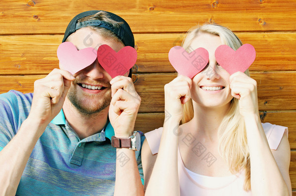 fall in love concept - young couple holding paper hearts over ey