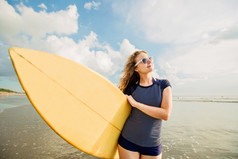 美丽年轻的白种人女孩在 rushwest 和太阳镜，黄色冲浪板在勒吉安海滩，巴厘岛。lyfestyle、 休闲、 运动、 度假、 幸福概念