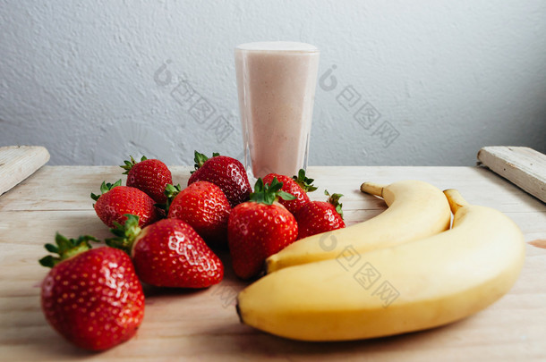 新鲜的草莓香蕉奶昔混合在木桌上