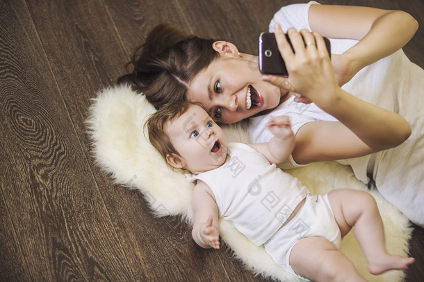 女人抱着一个婴儿做躺在地板上的自拍照