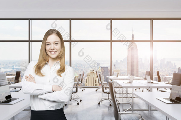 Smiling beautiful business lady with cross hands is standing in a modern panoramic office in New Yor