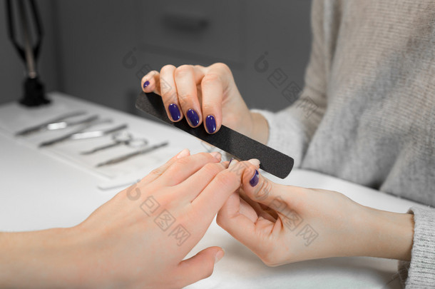 Manicure process with nail file in beauty salon