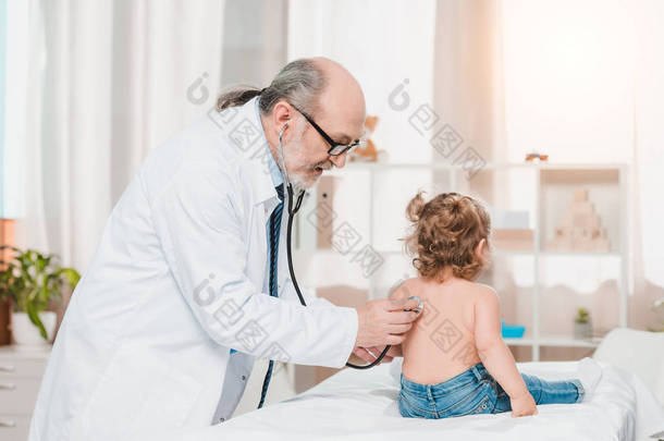 高级儿科医生穿着白大褂检查小女孩的听诊器在诊所