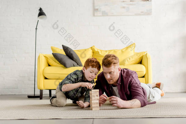 集中红头发的<strong>父亲和儿子</strong>躺<strong>在</strong>地毯上玩木块<strong>在家里</strong>