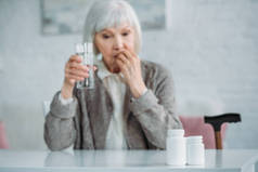 灰色头发妇女的选择焦点与玻璃水在家里服药