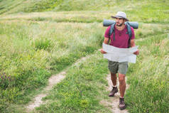 徒步旅行者在帽子与背包持有地图和走在路径上