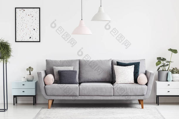 灰色沙发与枕头在白色公寓内部与<strong>海报</strong>和<strong>植物</strong>在橱柜。真实照片