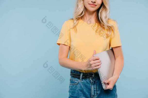 被裁剪的女孩在衬衣和短裤站立与笔记本电脑隔离蓝色