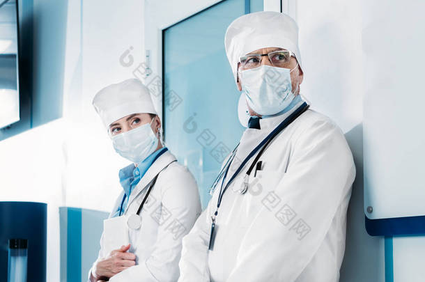 医用口罩中的男、女医生站在医院走廊里看着