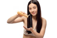 年轻的亚洲妇女的画像在手里倒洗发水在白色, 头发治疗概念