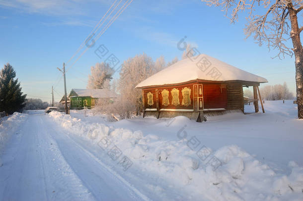 冬天的风景与土路, 冰冻树和木房子在乡下在日出。俄罗斯
