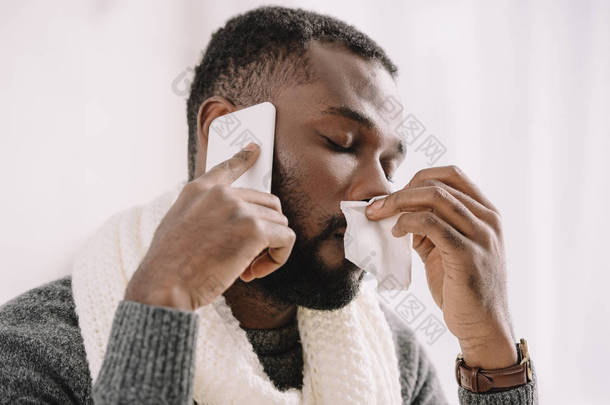 生病的非洲裔美国男子与流鼻涕拿餐巾, 而在智能手机上交谈