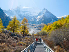 在中国四川亚丁自然保护区, 以雪山为背景的走在雪山人行道上的游客